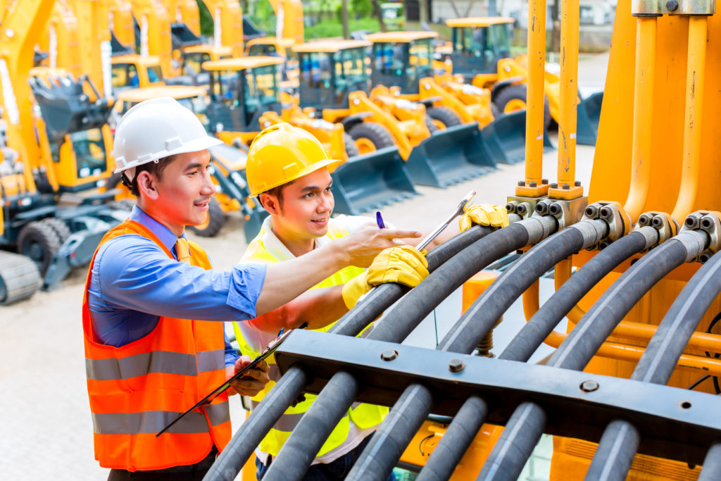 Asian motor mechanic discussing with engineer task list in construction machine workshop